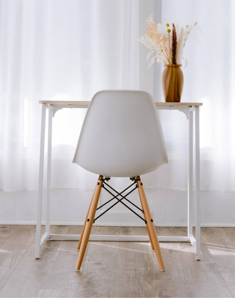 Chaise blanche en bois devant bureau minimaliste avec vase à fleurs, lumière naturelle.