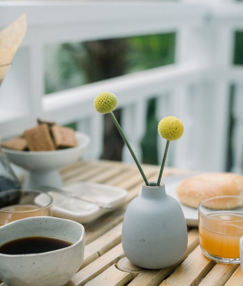 vase à deux fleurs jaunes, café, jus d'orange, petit pain, biscuits, balustrade.